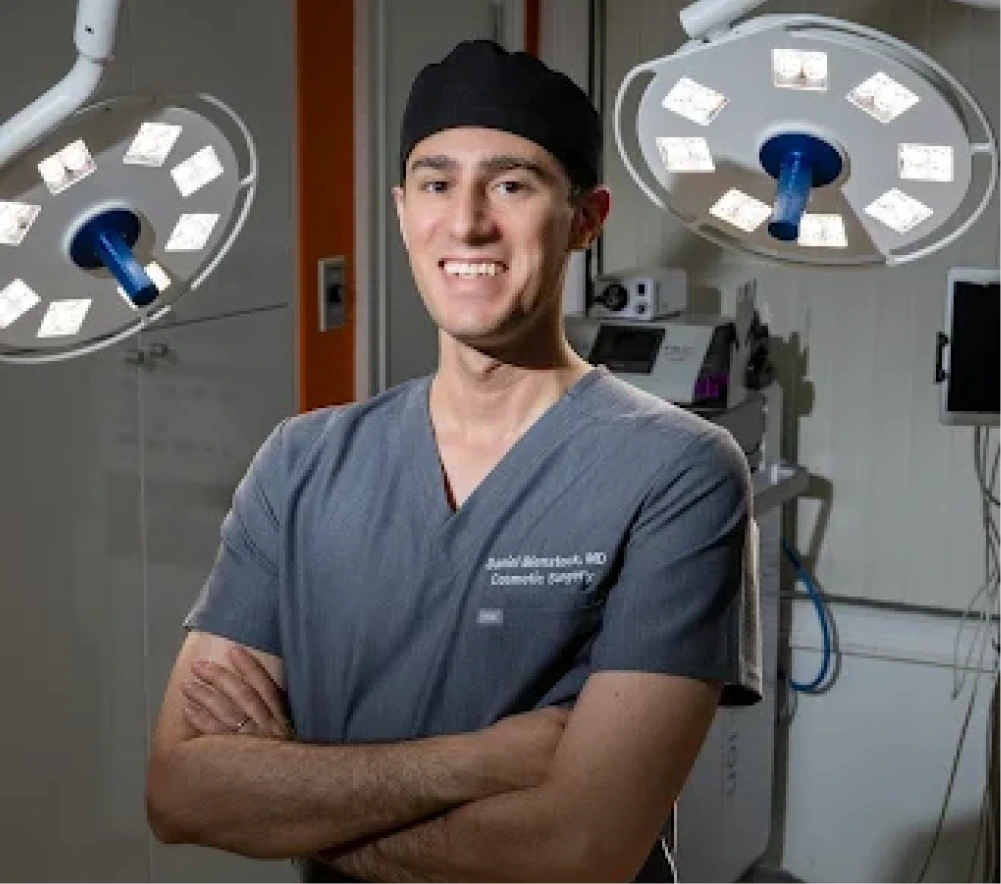 Surgeon in scrubs smiling in an operating room with overhead surgical lights