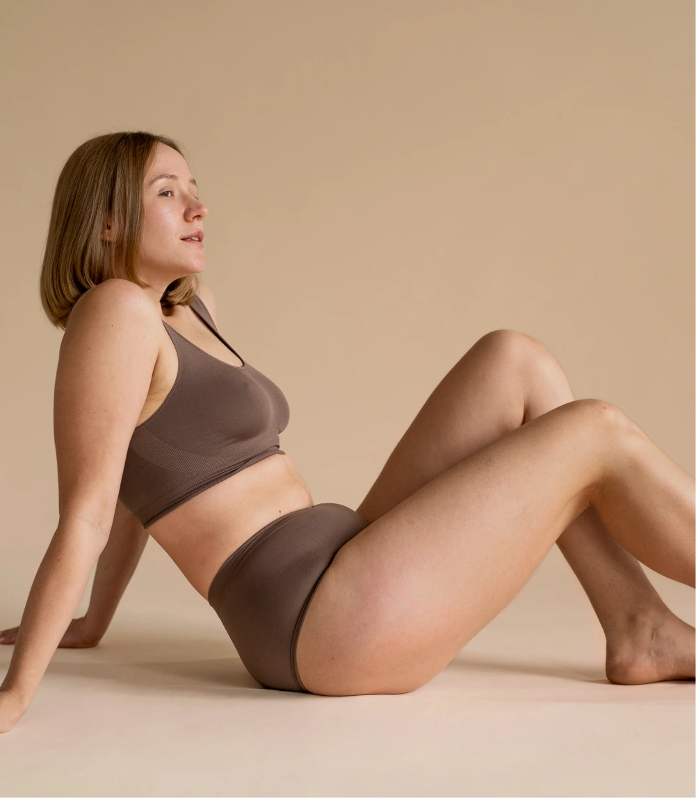 Woman in brown crop top and shorts posing to show body contouring results