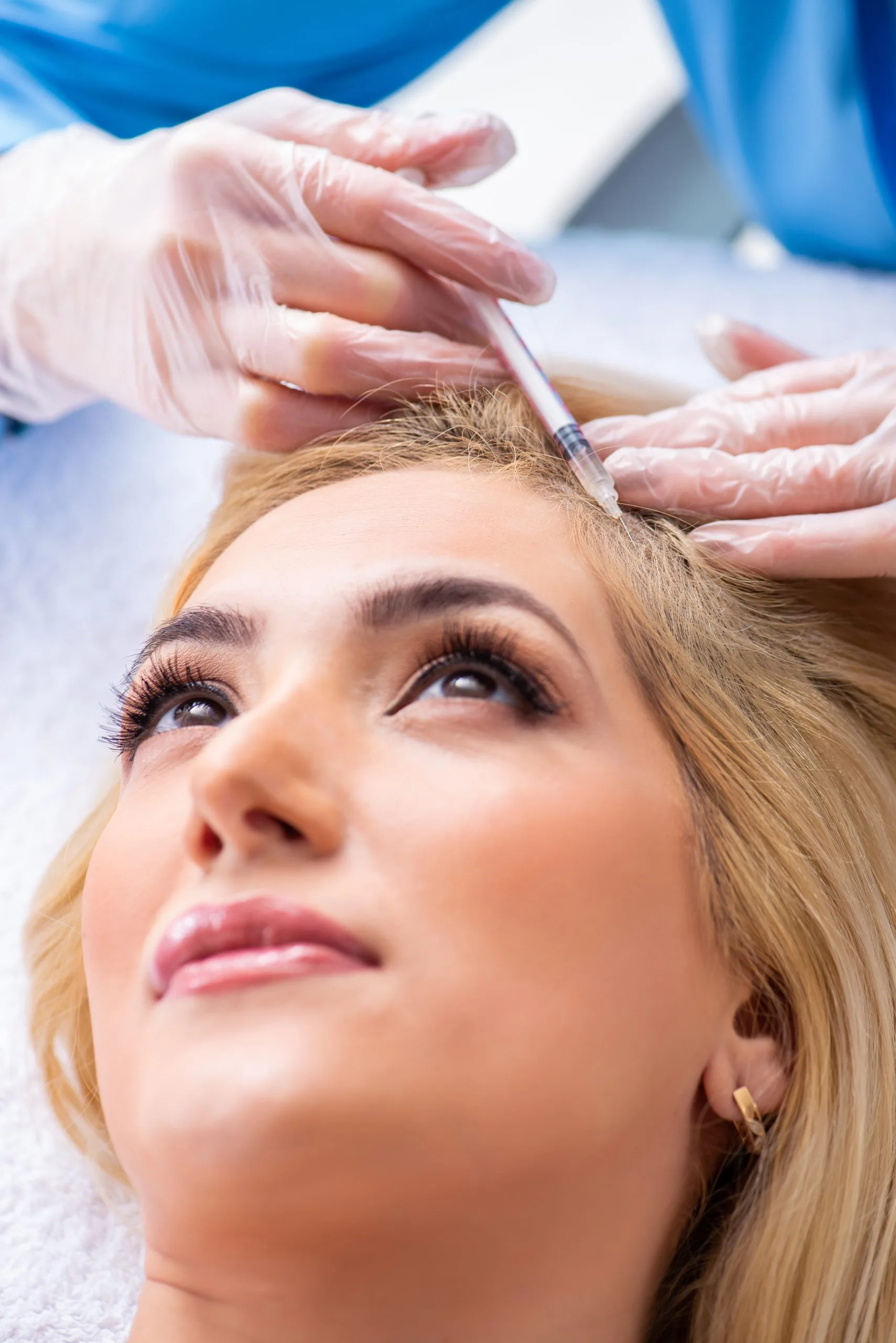 Doctor in surgical gloves and blue cap injecting forehead area of patient