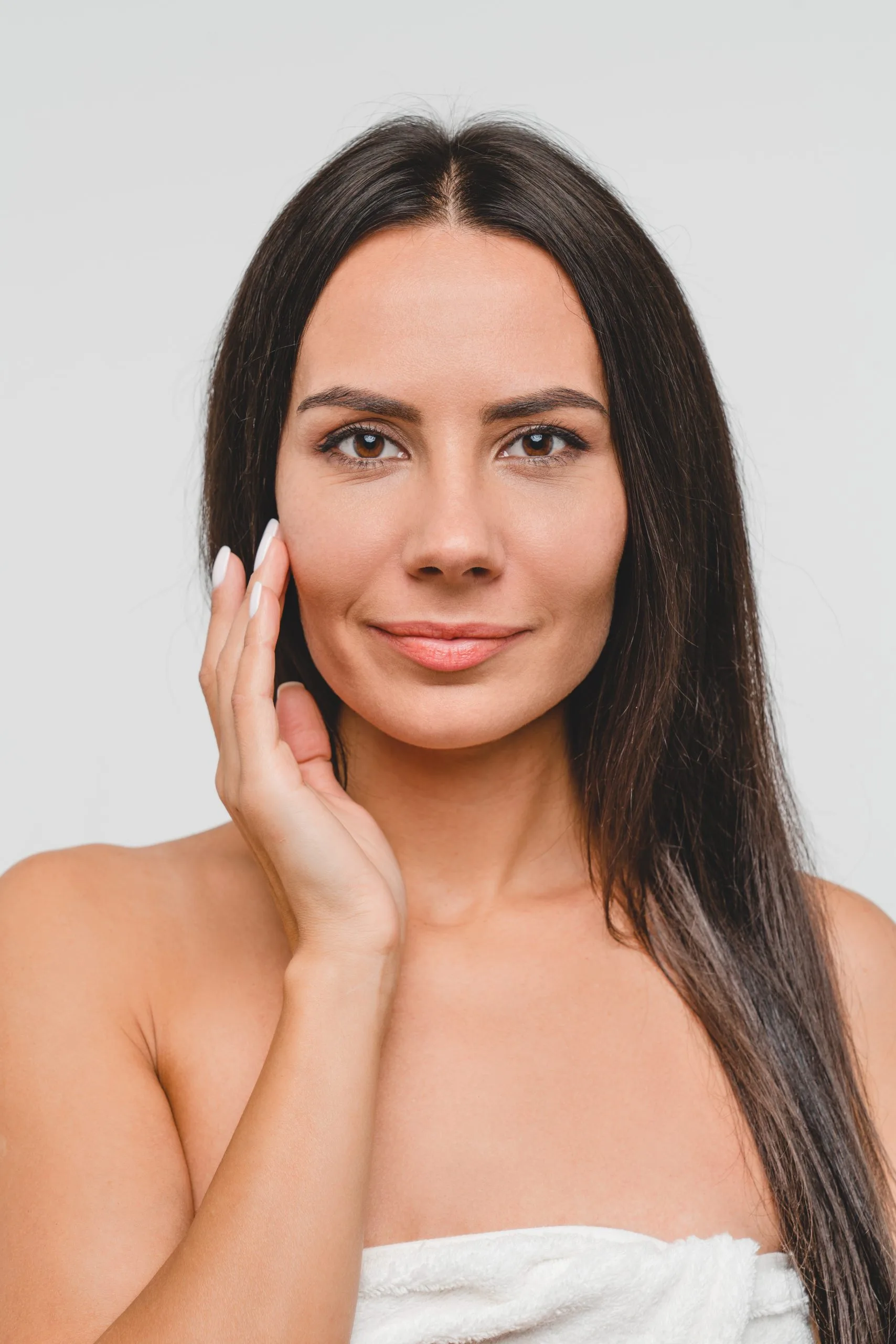 Woman with long dark hair touching her cheek, looking directly at camera