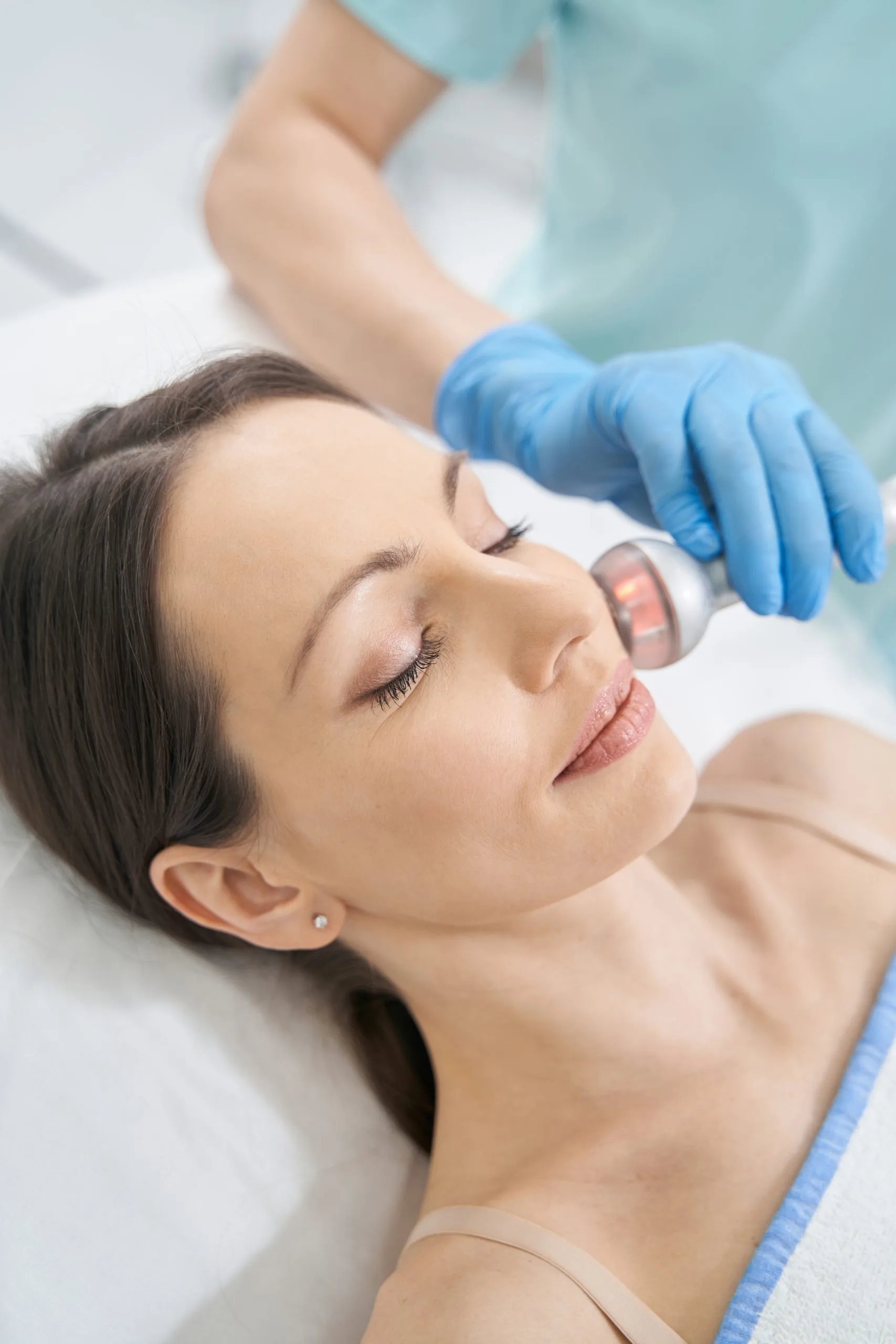 Practitioner in blue gloves using laser device on patient's face during treatment