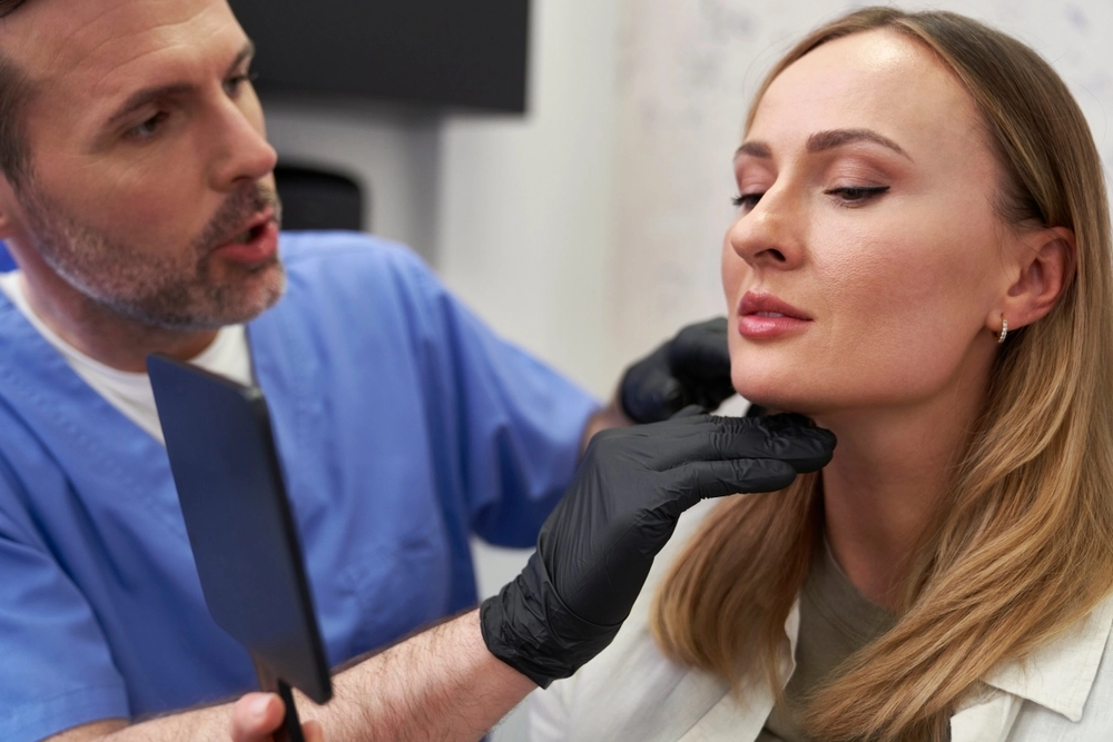 Doctor in blue scrubs examining a woman's jaw and face with gloved hands