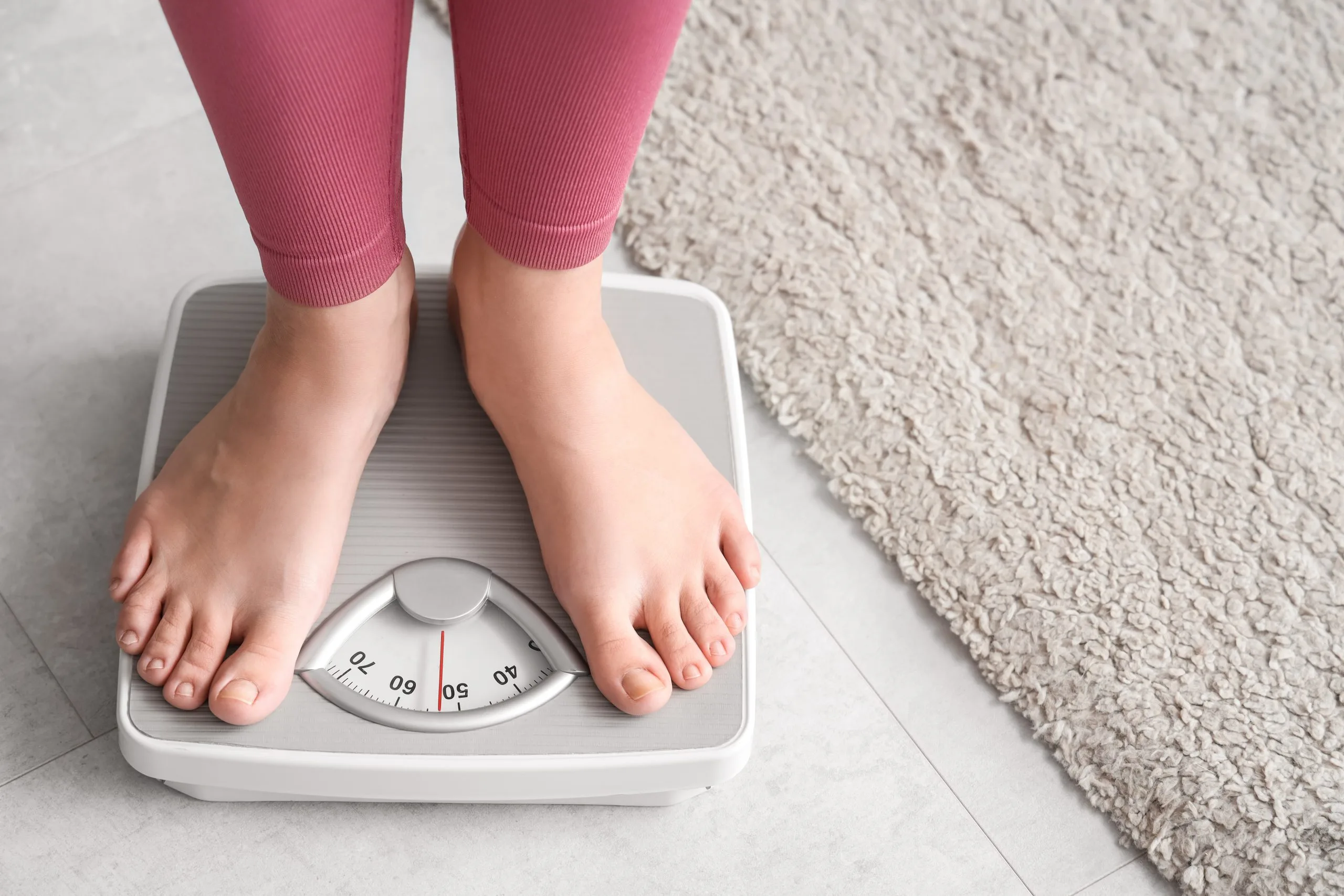 Person standing on bathroom scale wearing pink leggings