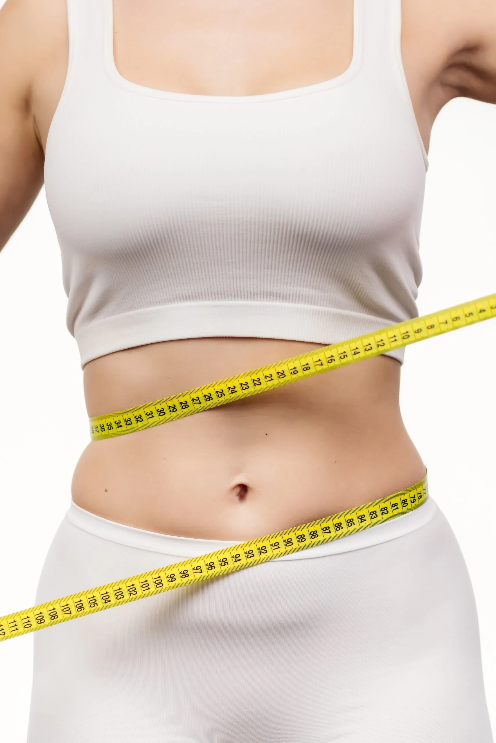 Woman measuring waist with yellow tape measure across abdomen and hips