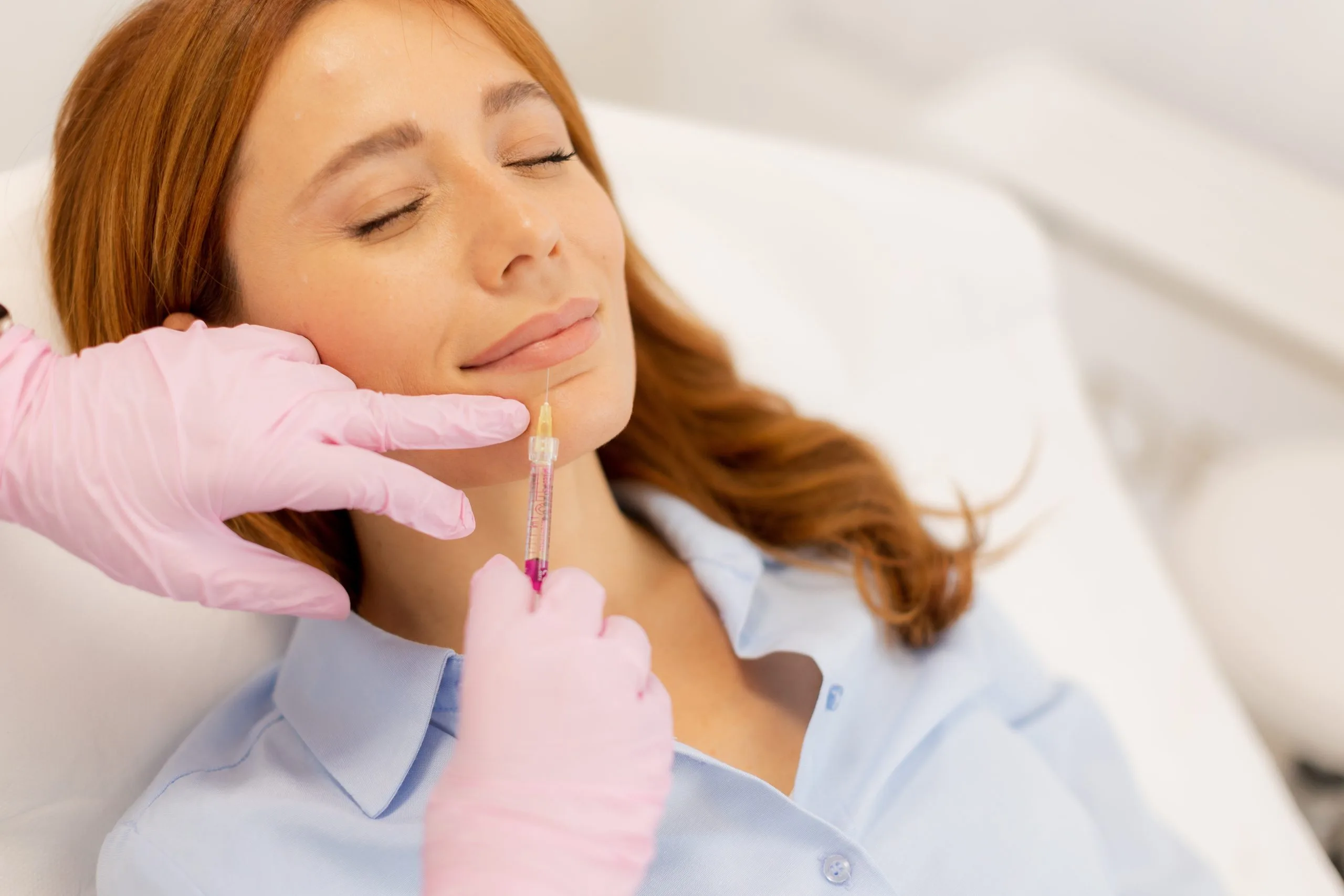Practitioner in pink gloves injecting filler into patient's cheek