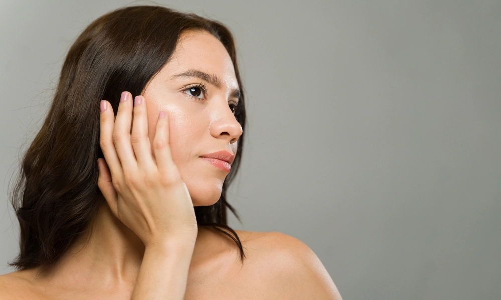 Woman in profile touching her face with hand against gray background
