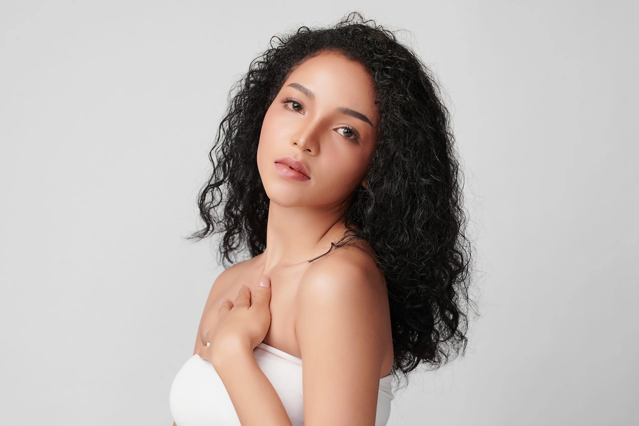 Woman with long curly black hair looking over her shoulder against neutral background