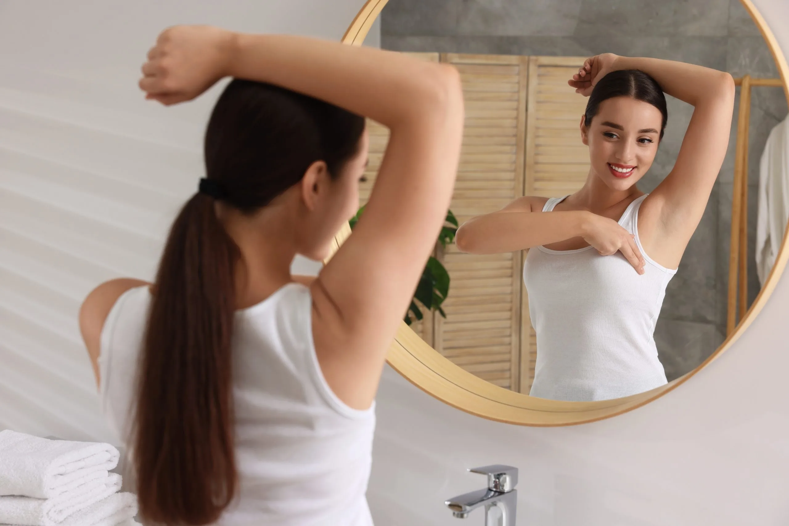 Woman with long brown hair examining her arm in round mirror