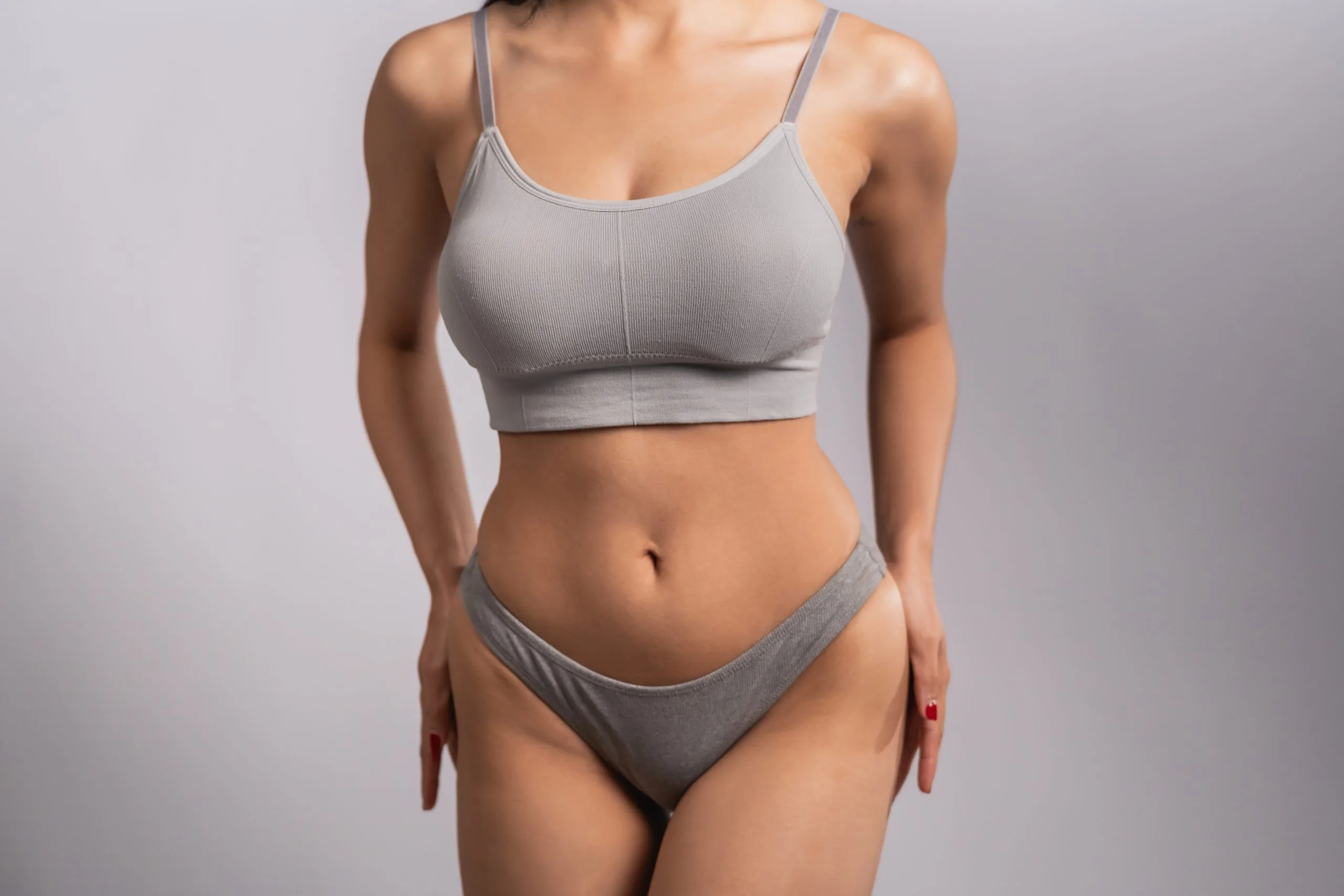 Woman in gray sports bra and briefs standing against neutral background